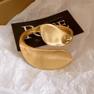 Close-up of matte gold twisted hollow bangle with artistic brushed metal texture details