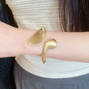 Detail shot of an irregular gold-colored matte finish open cuff bracelet on a wrist.
