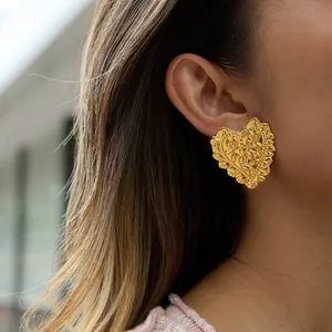 Nahaufnahme eines eleganten goldenen herzförmigen Ohrrings mit Blumengravur an einem Modell