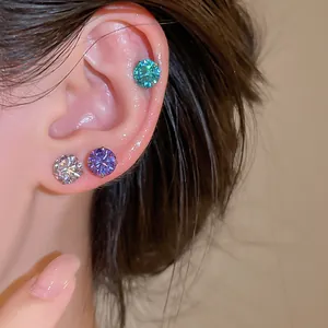 Détail de trois boucles d'oreilles clous en zircone étincelant de couleur sur une oreille