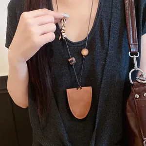 Gros plan d'un collier pendentif long en cuir porté sur un haut en maille noir