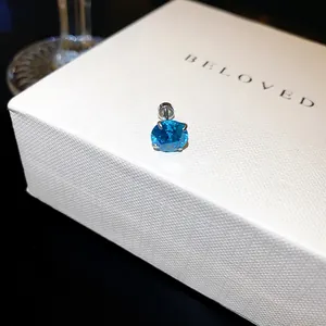Gros plan d'une boucle d'oreille en zircon bleu sur un coffret cadeau blanc avec fermoir à vis