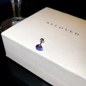 Détail d'une boucle d'oreille en zircon violet sur un coffret cadeau blanc texturé chic