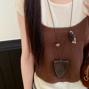 Gros plan d'un collier pochette à clés en cuir sur un haut en maille marron
