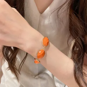 Detailed close-up of a vibrant orange resin oval bracelet with golden metal setting