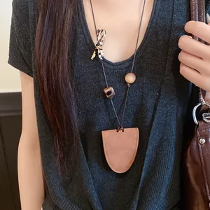 Détail d'un long collier à pendentif en cuir porté avec un haut noir en maille