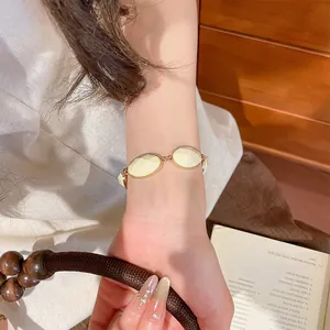 Close-up of vintage-style gold-tone bracelet with oval cream resin elements on wrist
