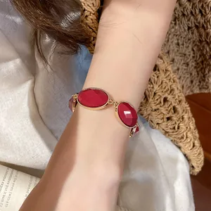 Close-up view of a vintage-style gold bracelet with red oval resin charms on a wrist