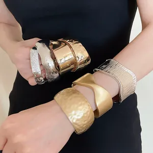 Stack of chunky metal cuff bracelets featuring hammered and pleated textures on a model