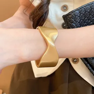 Elegant matte gold cuff bracelet featuring a unique wavy fold design worn on a female wrist.