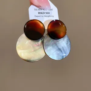 Detailansicht von Ohrringen mit bernsteinfarbenem Acetat und schillernden Muschelscheiben.