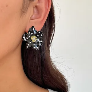 Vue détaillée d'une boucle d'oreille fleur à pois noirs avec perle sur un modèle