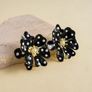 Gros plan de boucles d'oreilles fleurs en émail noir à pois blancs et perle centrale au cœur