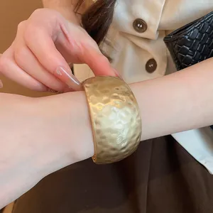 Detailed close-up of a matte gold hammered texture cuff bracelet on a model's wrist