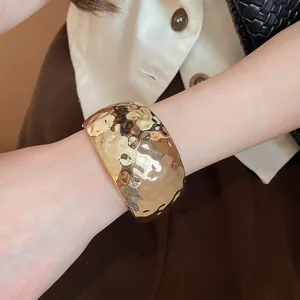 Macro detail of a stylish wide hammered gold cuff bracelet worn on a woman's wrist