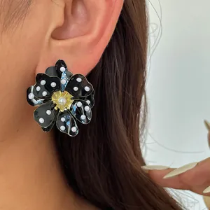 Détail d'une boucle d'oreille fleur en métal style noir avec pois blancs et centre perle