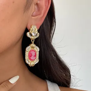 Close-up of a vintage-style gold earring featuring a pink cameo and sparkling rhinestone details