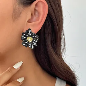 Gros plan d'une boucle d'oreille fleur à pois noirs et blancs avec centre en perle