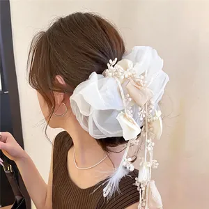 Vue détaillée d'un grand chouchou en organza blanc avec glands floraux et plumes