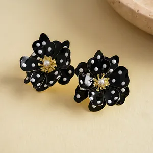 Détail macro de boucles d'oreilles fleurs noires avec pois blancs et perle centrale
