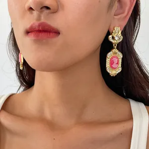 Close-up of vintage court style rhinestone earrings with pink resin cameo on model