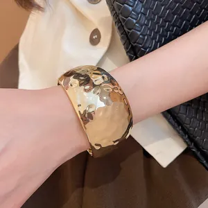 Detail of minimalist gold-toned hammered metal cuff bracelet worn on a female wrist.