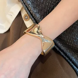 Close-up detail of a twisted gold metal cuff bracelet with a glossy reflective finish