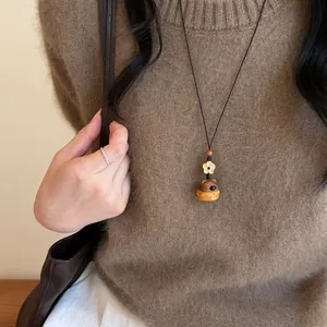 Détail d'un collier vintage avec pendentif éléphant en bois et fleur sur un pull marron.