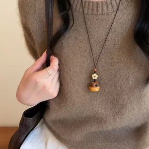 Vue détaillée d'un collier pendentif en bois fait main avec fleur et animal sur un pull brun.