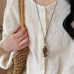 Collier pendentif éléphant en bois fait main, vue détaillée sur une chemise en lin beige.