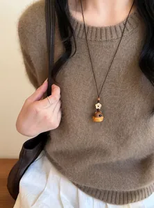 Gros plan d'un collier pendentif éléphant en bois fait main avec breloque fleur sur pull