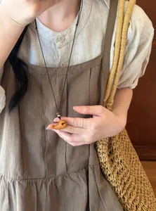 Gros plan d'un collier pendentif éléphant en bois rétro porté sur une robe en lin.