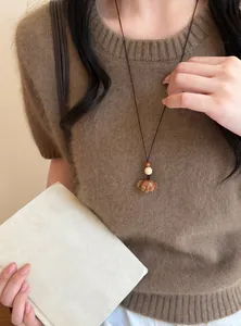 Gros plan d'un collier pendentif éléphant en bois fait main porté sur un pull marron