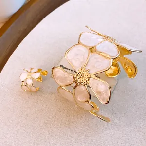Nahaufnahme von elegantem Goldmanschetten- und Ring-Set mit weißen Emaille-Blumen