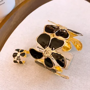 Detailansicht eines schwarzen Emaille-Blumen-Armreifs und passenden Rings in Goldoptik.