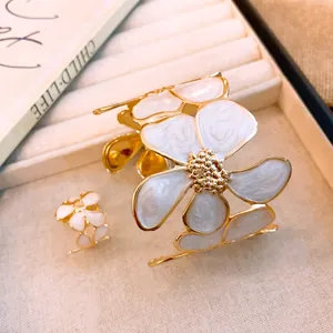 Detailansicht der goldfarbenen Blumenmanschette und des Rings mit weißer Emaille-Textur