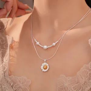 Detailaufnahme einer silberfarbenen doppelten Halskette mit Gänseblümchen und Perlen