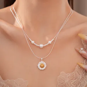 Detailansicht einer silbernen Doppelkette mit Sonnenblumenanhänger und weißen Perlen