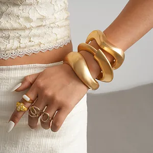 Detailed close-up of matte gold irregular twisted geometric bangles and rings on wrist