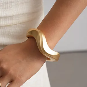 Close-up view of a minimalist matte gold irregular twisted geometric bangle bracelet on wrist