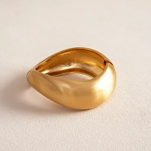 Detail macro view of matte gold irregular twisted geometric bangle on textured surface