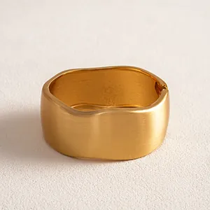 Macro detail of a wide matte gold irregular geometric bangle with a brushed finish