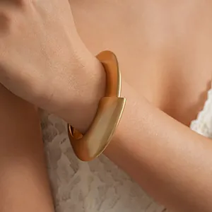 Close-up detailed view of a matte gold irregular twisted geometric bangle on a model wrist