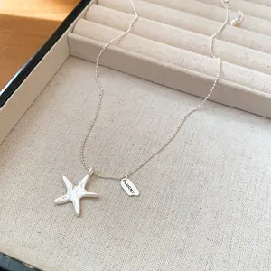 Detailed view of a silver starfish pendant necklace featuring a LUCKY tag in a jewelry tray
