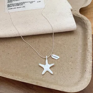 Close-up of a silver starfish necklace with a 'LUCKY' tag on a neutral background.