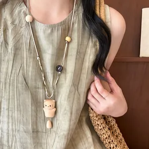 Artistic wooden cat pendant necklace on a long leather cord worn over a green linen dress