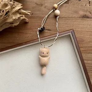 Detail shot of a cute handmade wooden cat pendant on a white and brown cord necklace.