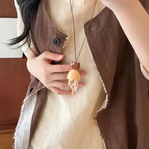 Close-up of a unique wooden cat jellyfish pendant necklace worn with a brown vest