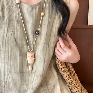 Detailed view of a handmade wooden bear pendant necklace on a textured linen dress.