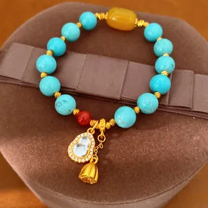 Detailansicht des vergoldeten Hulu-Anhängers und der türkisfarbenen Perlen am Armband.
